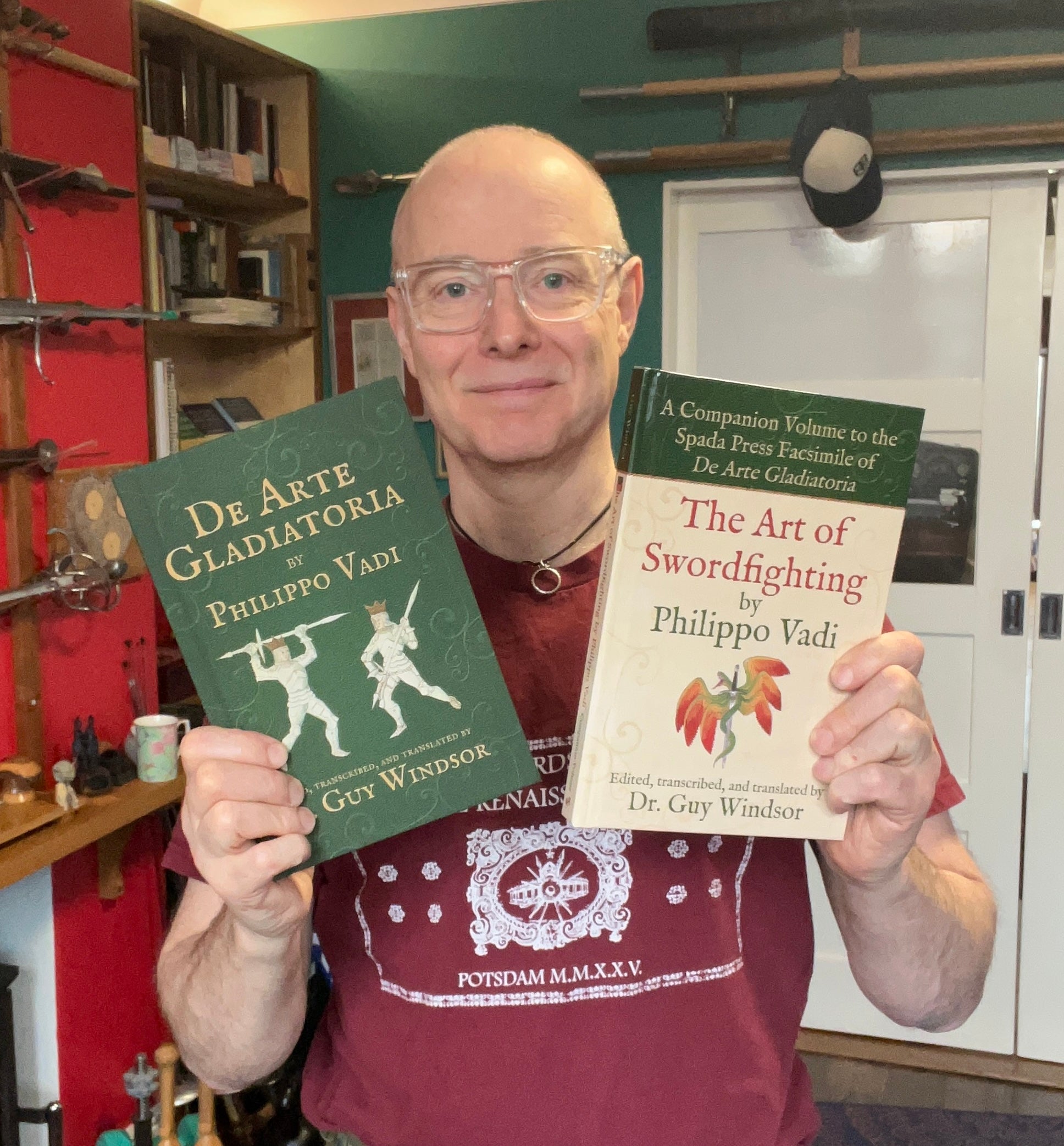 Guy Windsor holding two books titled 'De Arte Gladiatoria' and 'The Art of Swordfighting' by Philippo Vadi.